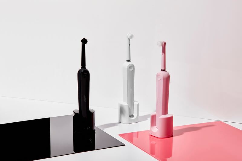 a black toothbrush, a white toothbrush, and a pink toothbrush sit on black, white, and pink tiles